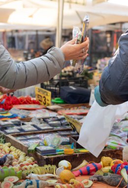 Kadın, açık hava sokak pazarından erkeklerden mal alıyor.
