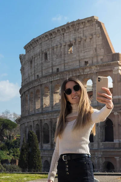Ung glad kvinde tager en selfie med telefonen foran det romerske colosseum - Stock-foto