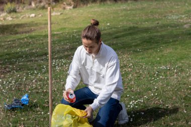 Genç adam çim parkındaki insan kirliliğini toplamak için çömeldi.