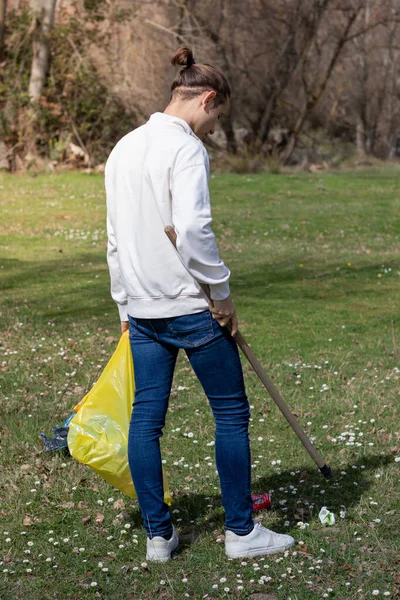 Homme bénévole ramassant les ordures avec l'outil de ramassage d'un champ fleuri marguerite — Photo