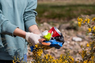 Çiçekler arasında bulunan çöpü gösteren tanınmamış bir kadın.