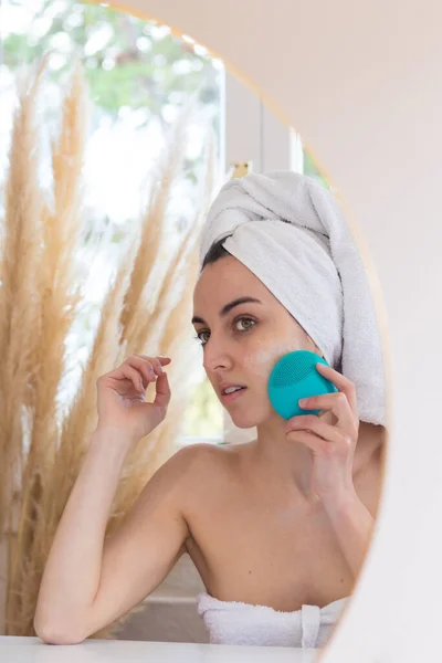 Woman cleaning skin with ultrasonic device during morning hygiene procedures