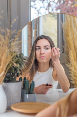 Güzel bir kadın makyaj yaparken kaşlarını boyuyor.