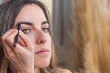 Sarı ve bal gibi gözleri olan kadının makyaj yaparken kaşlarını boyadığı yakın plan.