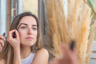 Evinde kaşlarını fırçalayan ve dolduran güzel genç bir kadının ön görüntüsü.