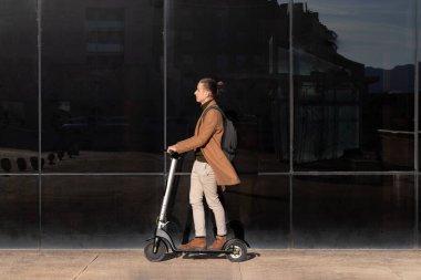 Genç işadamı arka planında parlak siyah bir bina olan elektrikli scooter üzerinde çalışacak ve etrafındaki boşluğu kopyalayacak.