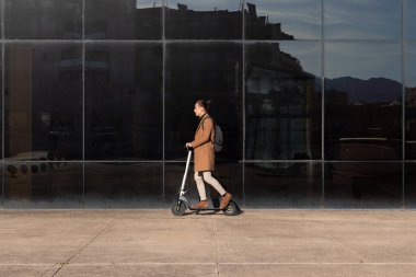 Çevresel kirliliği önlemek için elektrikli scooterlı büyük bir şehirde işe gidip gelen genç bir adamın yan görüntüsü