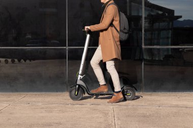 Her gün işe gidip gelen tanınmamış bir iş adamı mikro scooter kullanıyor ve kahverengi ve modern bir kıyafet giyiyor.