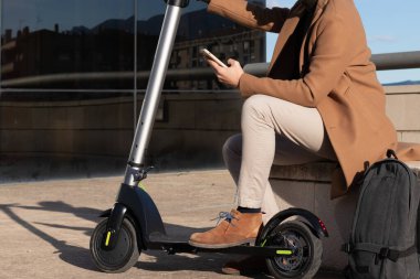 Şehir caddesinde elektrikli scooter için akıllı telefon kiralama uygulaması kullanan bir adam. Modern ulaşım ve ulaşım teknolojisi.