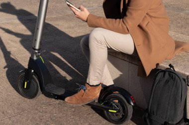 Tanımlanamayan kırpıcı, güneş ışığıyla işe gitmeden önce telefondaki elektrikli scooter uygulamasını çalıştırıyor.