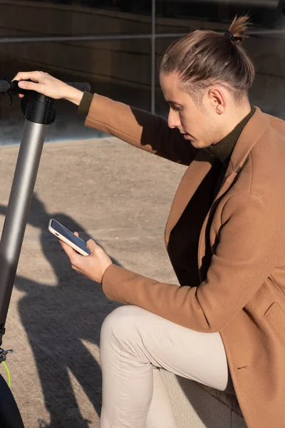 Jeune homme assis en activant l'application scooter électrique sur le smartphone pour le rouler autour du centre-ville — Photo