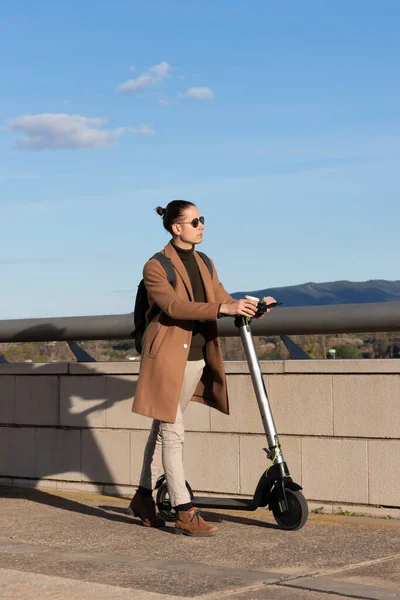 Vertical view of young handsome man with bun hairsyle walking with his electric scooter as and alternative transport — Photo