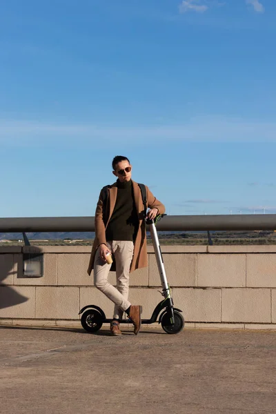 Vue verticale du jeune homme d'affaires se reposant du travail en profitant d'une tasse de café à l'extérieur avec un scooter électrique loué — Photo