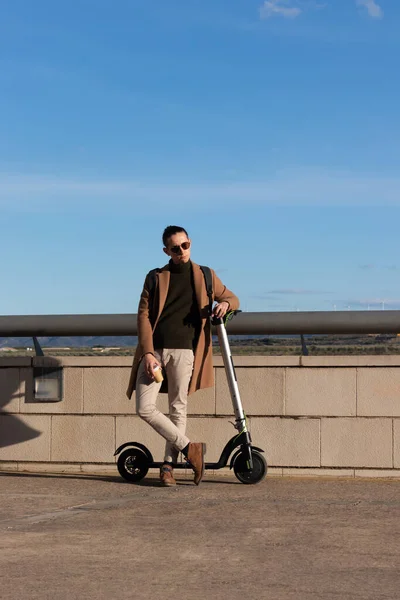 İşten dinlenen genç işadamının dikey görüntüsü. Kiralık elektrikli scooterla dışarıda bir fincan kahvenin tadını çıkarıyor. — Stok fotoğraf