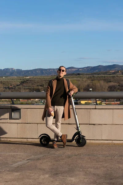 Genç ve yakışıklı bir adam kışın güneşli bir günün keyfini çıkarırken sıcak bir kahve ve gezmek için elektrikli bir scooter ile... — Stok fotoğraf