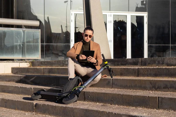 Jeune homme d'affaires beau assis sur les escaliers dans le quartier financier avec scooter électrique qui utilise pour se rendre au travail — Photo