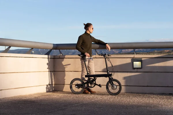 Young man using a folding electric bicycle to move in the city where he lives and be greener with the environment — Photo