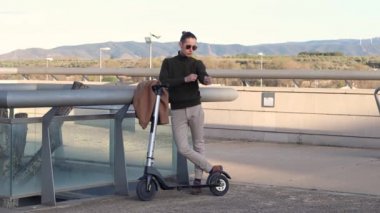 Genç adam şehir parkında elektrikli scooterla hareket eden akıllı adam kullanıyor.