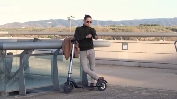 Young man using smartwatch moving with electric scooter in the city park — Vídeos de Stock