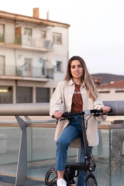 Retrato vertical de jovem olhando para a câmera segurando uma bicicleta elétrica em um ambiente urbano — Fotografia de Stock