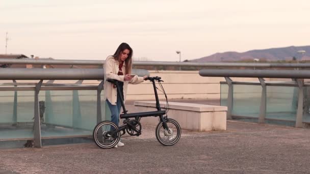 Young woman leaning on electric bike on her smarthphone waiting for her friend — Vídeo de stock