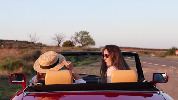 Side view of beautiful young women having fun driving on a red convertible car — Stockvideo