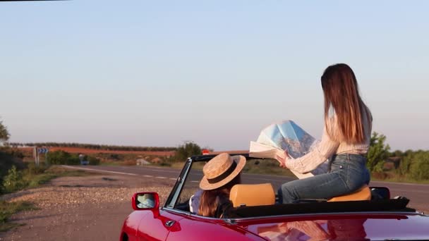 Women reading a map sitting in red convertible car on remote road — Vídeo de stock
