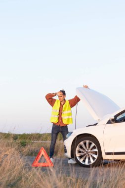 Yelekli genç adamların dikey fotoğrafı. Önünde bozuk arabasıyla yolda yardım arıyorlar.