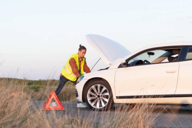 Yeni arabasında genç bir delikanlı. Yol kenarında kırık bir araba var. Yardım gelmesi için suluyor.