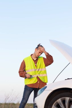 Sorunları olan yorgun bir adam açık kaputlu bozuk bir arabayı tamir etmeye çalışır ve etrafını kopyalamaya çalışır.