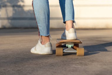 Şehir parkında kaykaylı kaykaycısını beyaz bir duvara karşı spor ayakkabı ve kot giyerken gördüm.