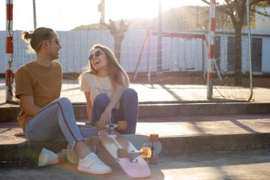 Genç Latin çift, kaykay sürdükten sonra şehir parkında eğleniyor ve gülümsüyor.