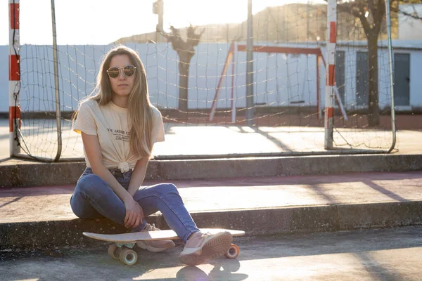 Young latin woman sitting on a stair step relaxed at the park with a skate board under her leg on street style outfit — Fotografia de Stock