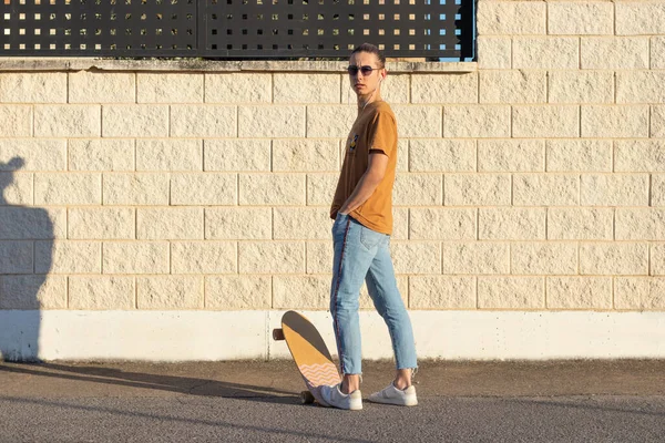 Sırtı dönük bir genç kameraya bakıyor güneş gözlüklü sörf tahtası ve kostüm hayatından zevk alıyor.