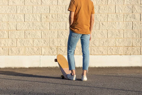 Sırtüstü yatmış genç bir adam kaykay kayıyor ve bahar günü beyaz tuğla bir duvara yaslanıyor.