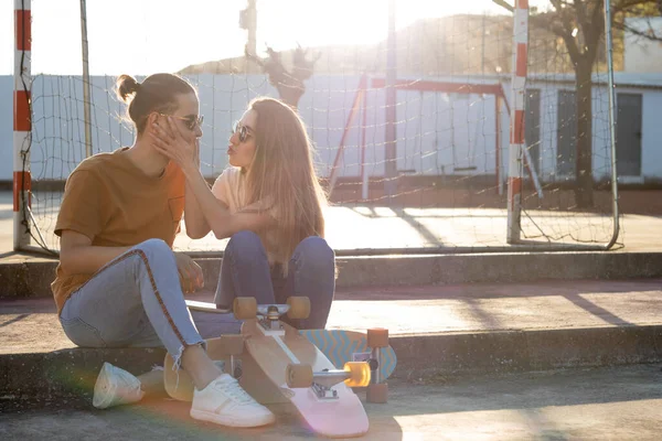 Cute young teenage couple having fun and joking with skate board around at sunset with flares around — Fotografia de Stock