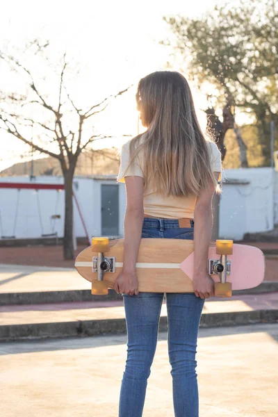 Zadní portrét štíhlé mladé blondýny drží přírodní vintage skateboard za zády — Stock fotografie