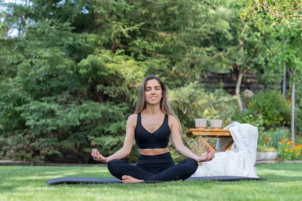 Vista frontal de una joven practicando la pose de loto y relajándose en el jardín verde mientras disfruta haciendo yoga — Foto de Stock