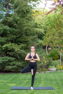 Yoga yapan genç bir Yogi kadını Vrksasana egzersizi, ağaç duruşu, spor kıyafetleri giyerek spor yapıyor.