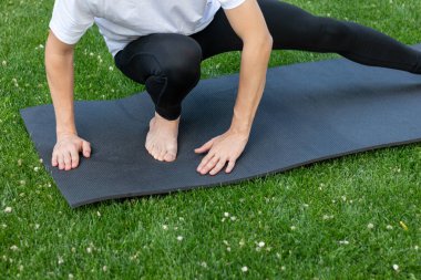 Bacak kaslarını esnetirken bahçede siyah bir paspasın üzerinde yoga yapan tanınmayan bir adamın yakın görüntüsü.