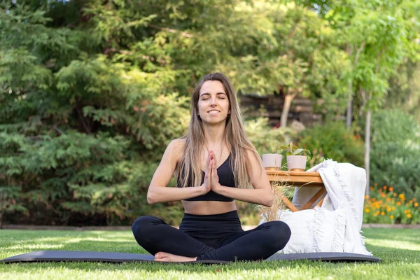 Mujer optimista sonriente y feliz practicando yoga al aire libre con una esterilla en el jardín con decoración boho — Foto de Stock