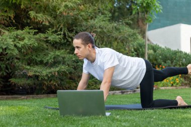 Young handsome man on sportswear concentrated while practising yoga following an online lesson on the internet