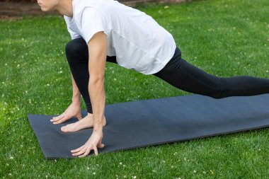 Geri dönüşü olmayan genç adam, siyah tayt giyerek bahçede düz bacakla yoga yapıyor.