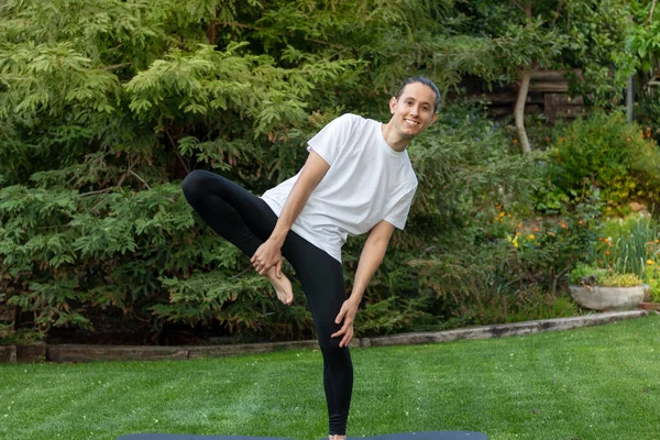 Joven cayendo tratando y aprendiendo a hacer una pose de yoga en el jardín para divertirse usando ropa deportiva — Foto de Stock