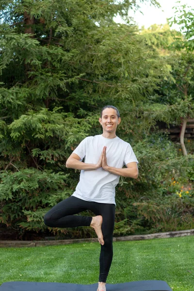 Joven sonriendo intentando y aprendiendo a hacer una pose de yoga en el jardín para divertirse vistiendo ropa deportiva — Foto de Stock