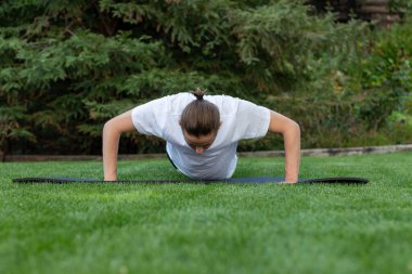 Young fit hipster man on a bun hairstyle doing push ups as daily exercise in nature in a park