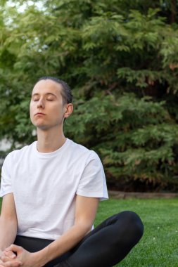 Young man with eyes closed taking deep breath from fresh and clean air sorrounded by nature in a park