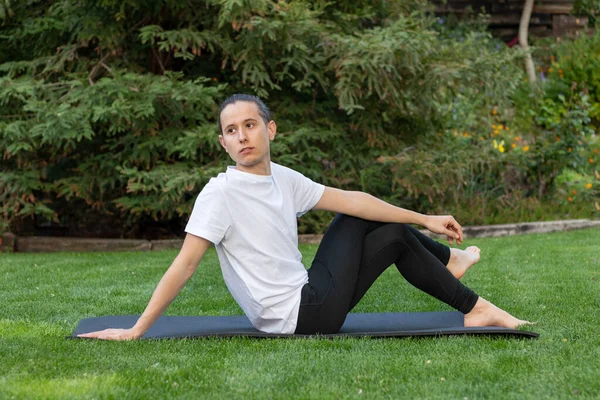 Hombre joven y hermoso que se estira después de haber hecho ejercicio de yoga mirando hacia un lado en una estera en el jardín — Foto de Stock