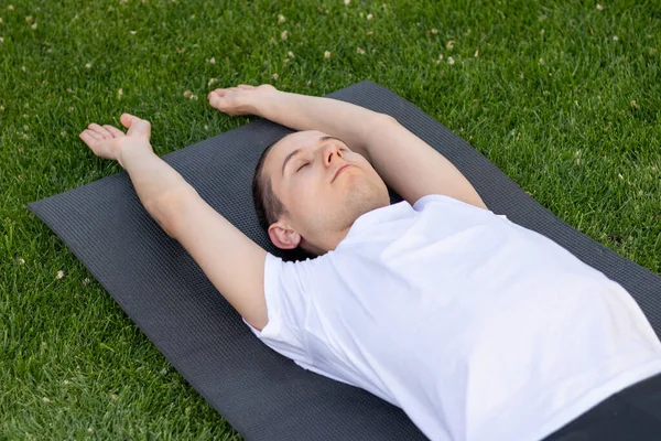 Joven hombre estirando su estante en una esterilla de yoga negro con los brazos extendidos. Ojos cerrados y respiración limpia aire fresco — Foto de Stock