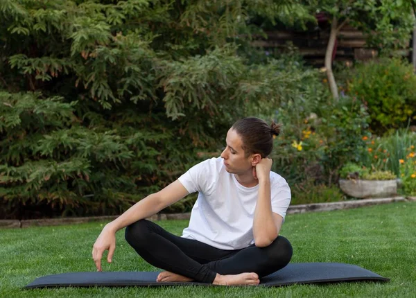 Niño adolescente mirando a un lado con las piernas cruzadas en una estera de yoga en el jardín o parque al aire libre en la naturaleza — Foto de Stock